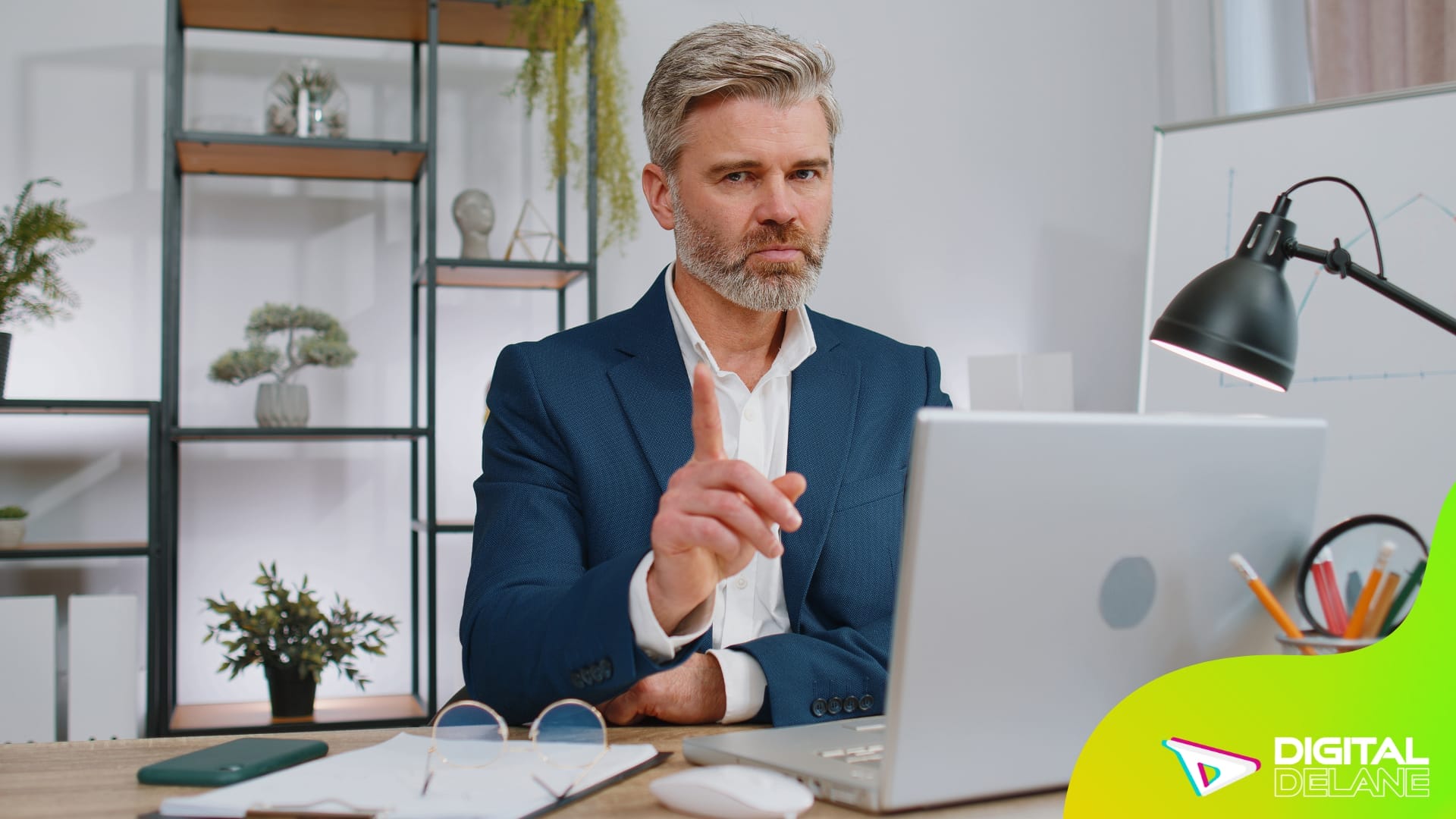 A man in a suit sits at a desk with a laptop, focused on his work in a professional setting.
