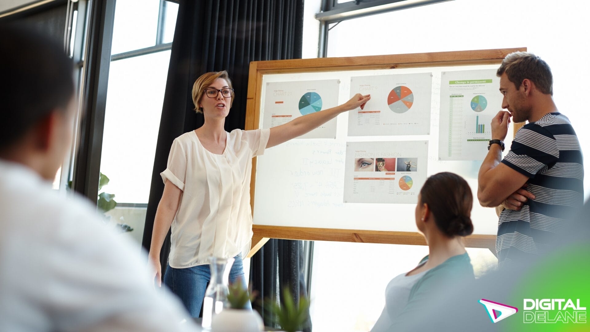 A woman points to a whiteboard while a group of people observes, discussing advanced analytics and AI-driven insights.