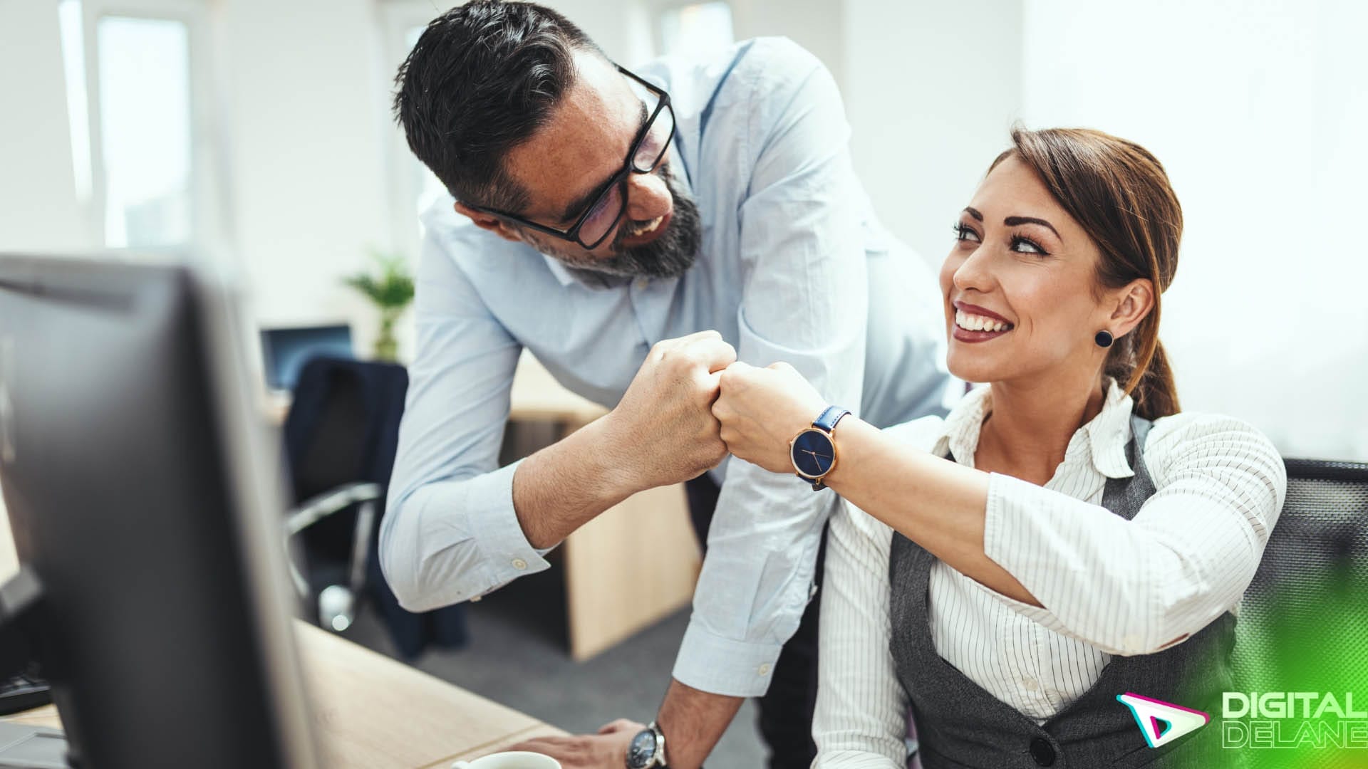 A man and woman smile at each other while collaborating on a computer, showcasing teamwork and engagement in a professional setting.