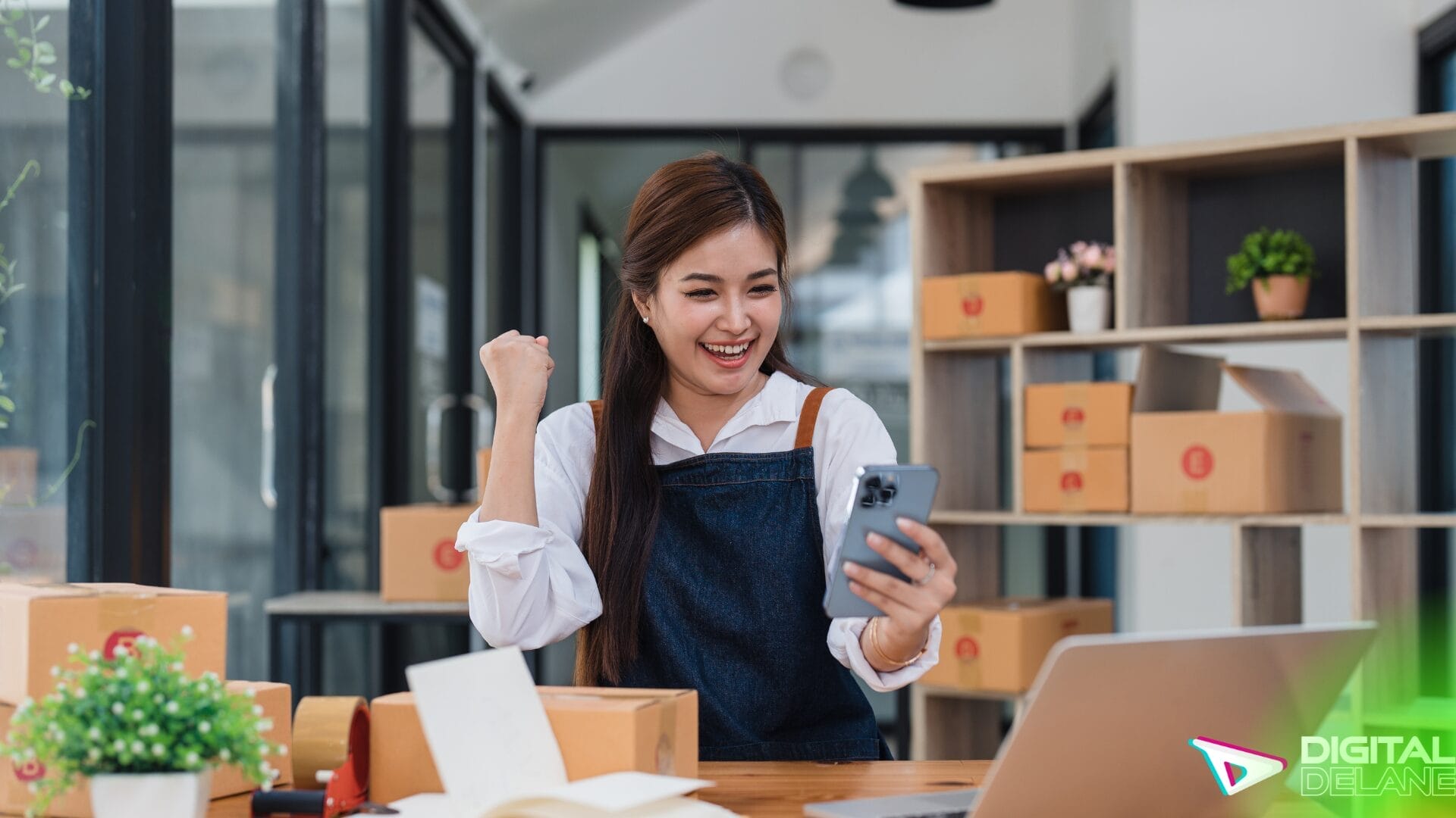A woman smiles while holding a laptop at a desk surrounded by boxes, embodying a positive work environment.